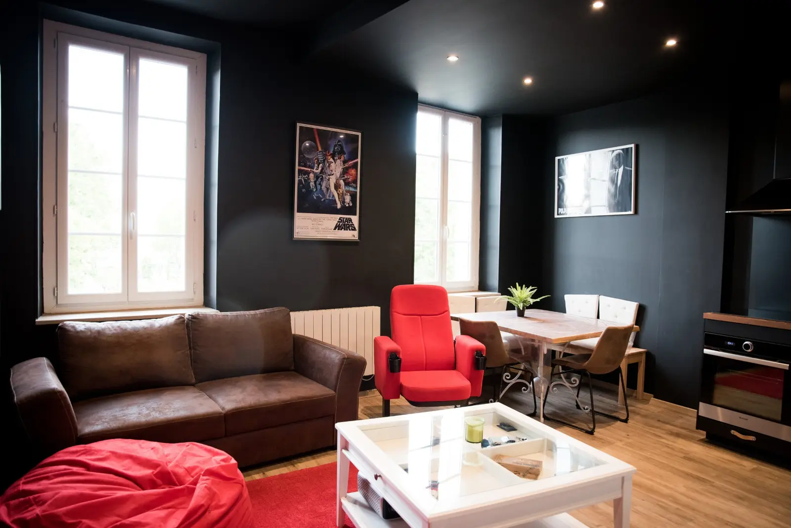 Salon aux murs noirs avec affiches de films, canapé et fauteuil de cinéma rouge