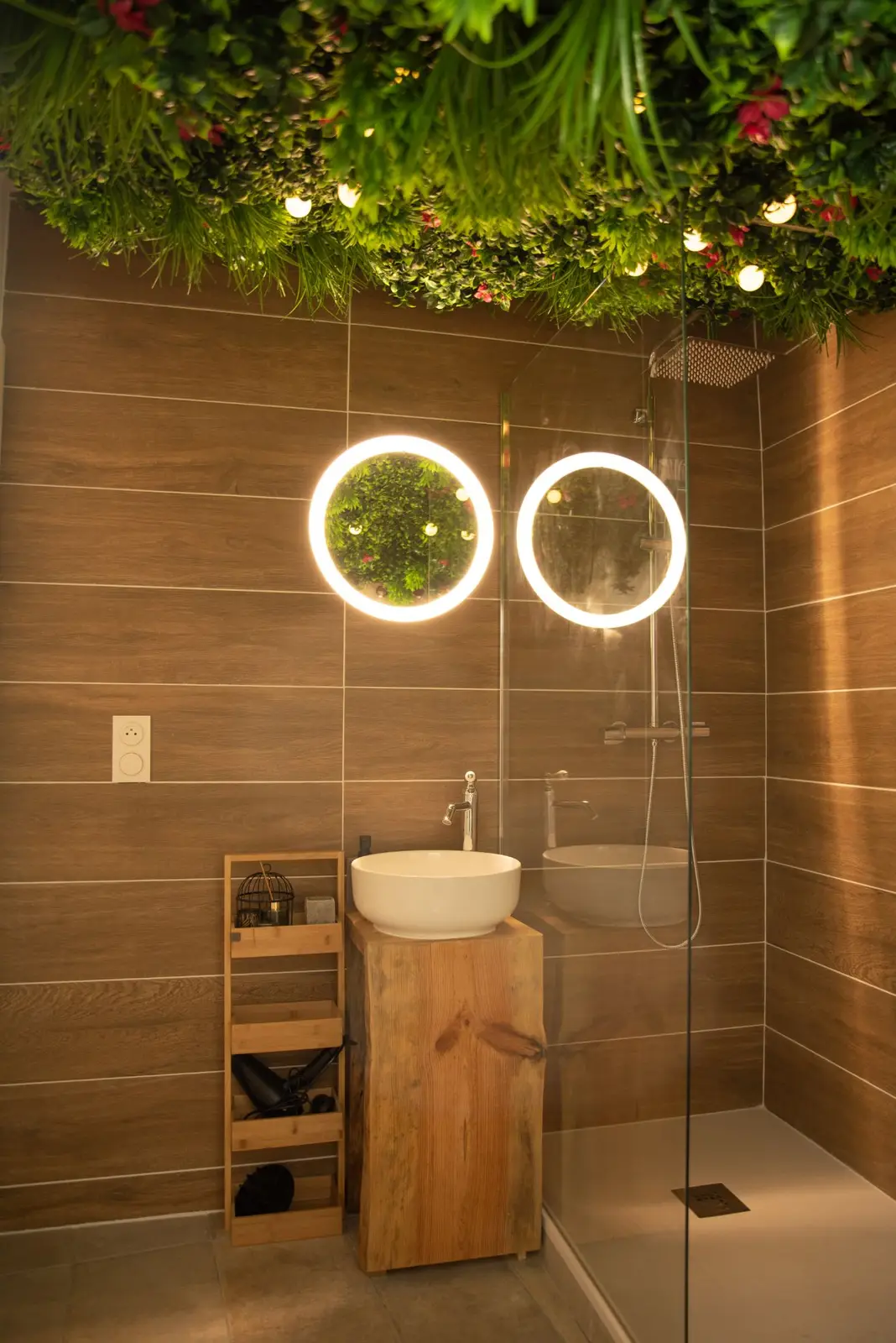 Salle de bain : plafond végétal illuminé, vasque sur tronc et miroirs ronds lumineux
